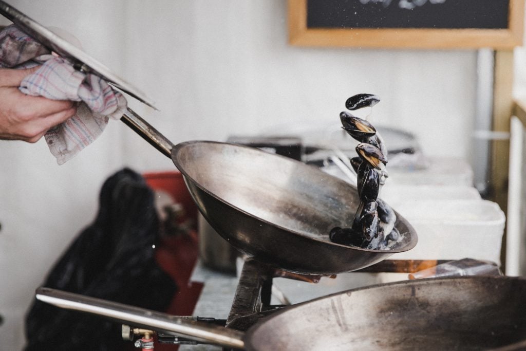 a hand tossing seafood out of a saute pan.