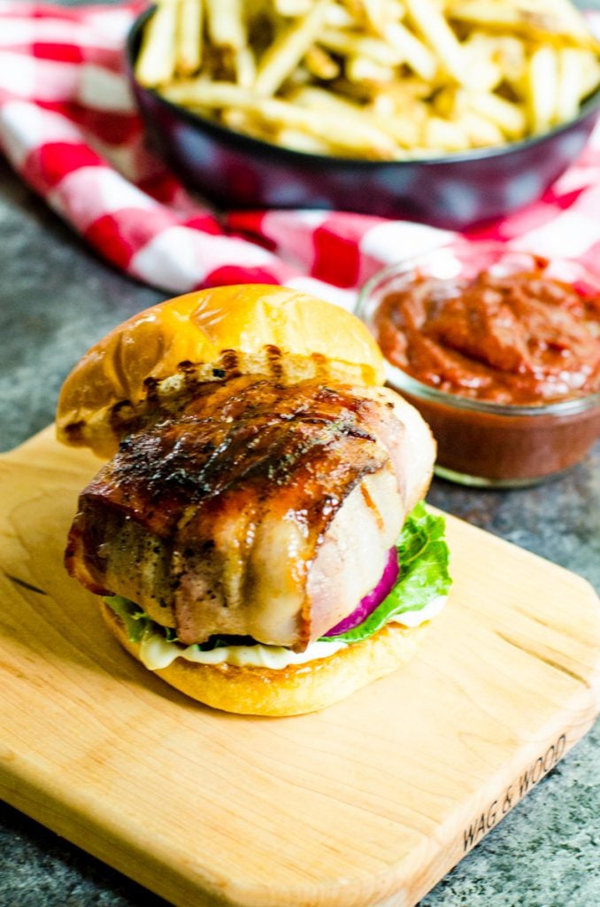 Grill marks on a burger thats on a cutting board in front of french fries and ketchup.