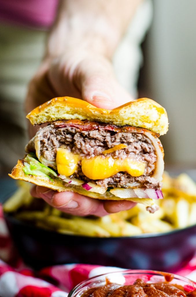 Cheese oozing out of a stuffed bacon wrapped burger.