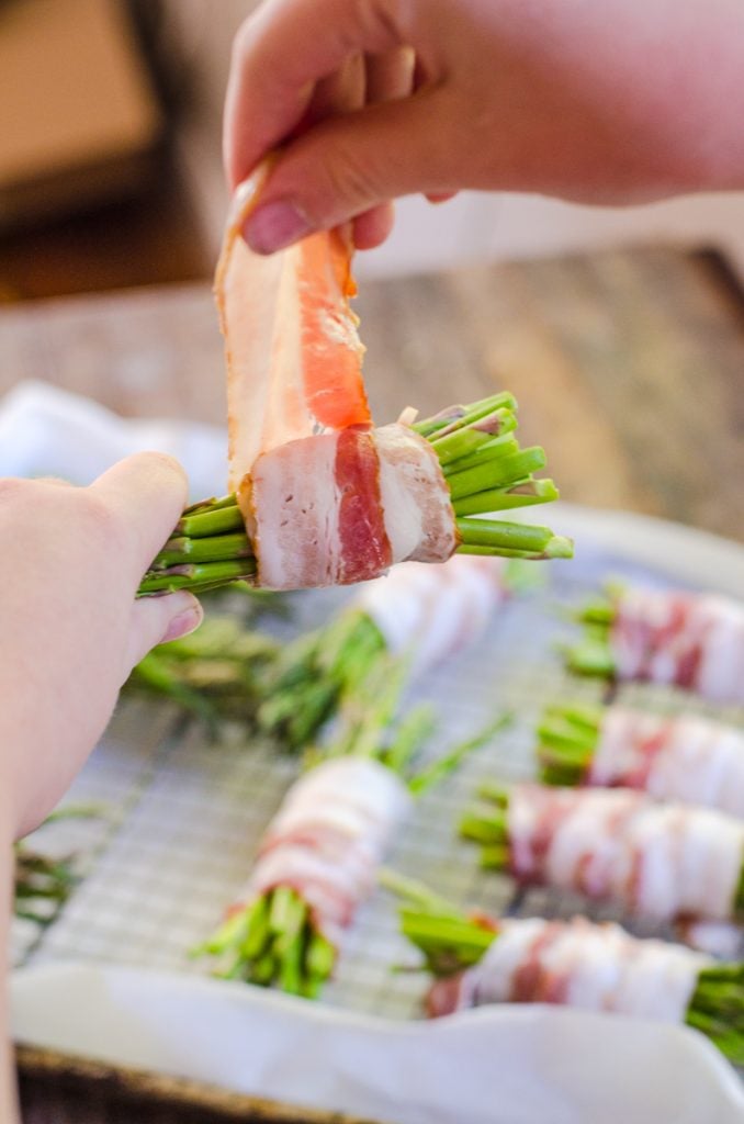 A hand wrapping bacon around an asparagus bundle.
