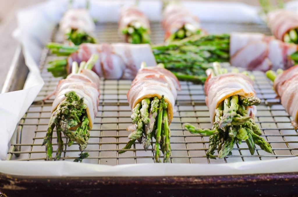 Multiple bundles of bacon wrapped asparagus on a baking rack.