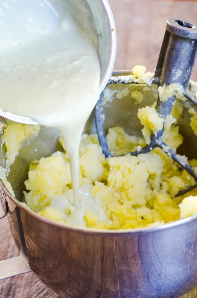 A blue cheese cream sauce being poured into cooked mashed potatoes.