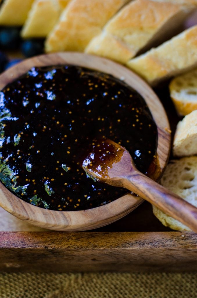 A wooden bowl of fig jam surrounded by sliced baguette.