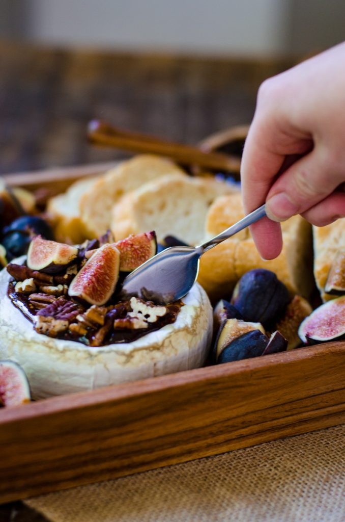 A hand using a cheese knife to slice open baked brie.