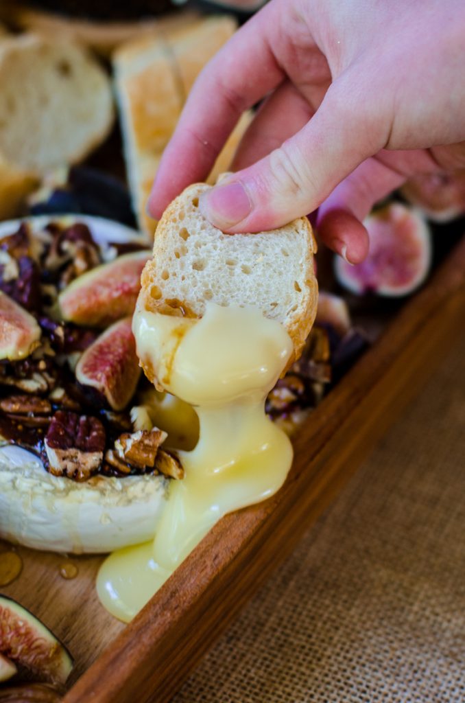 A hand using bread to dip into baked brie with fig jam.