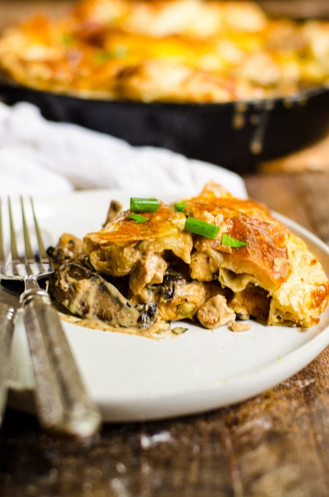 A slice of chicken and mushroom pie on a plate with a fork and knife.