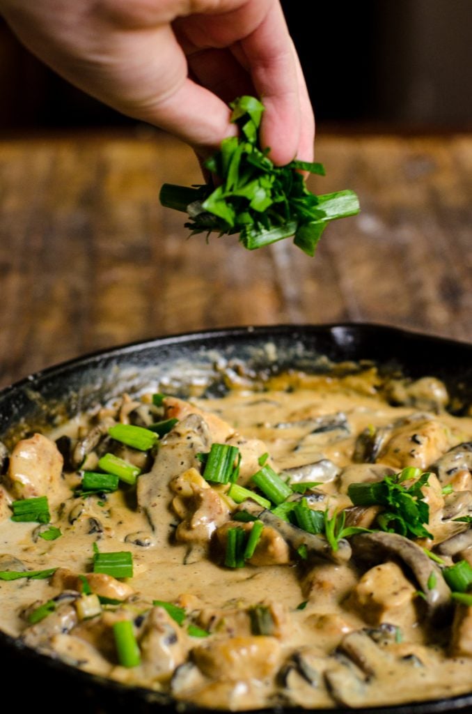 A hand sprinkling parsley and green onions into a pan.