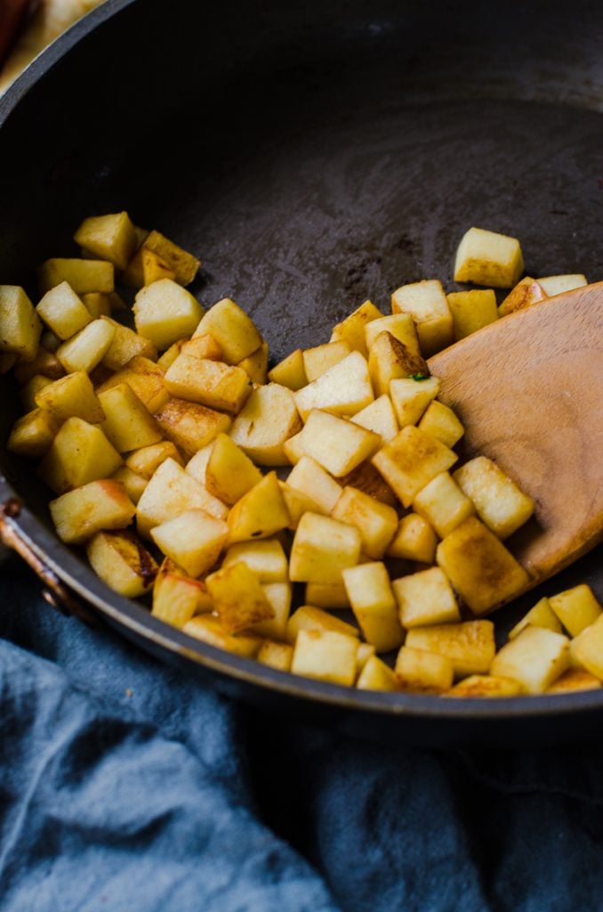 A spatula moving around cooked nutmeg diced apples in a nonstick pan.