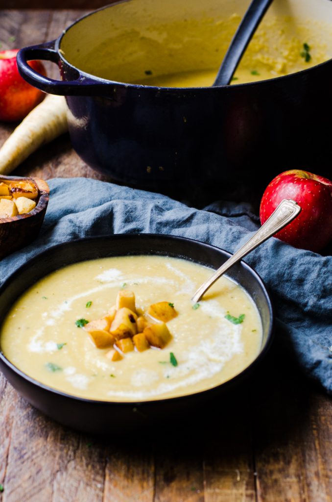 bowl of parsnip soup with apples next to the pot it was cooked in and a blue napkin.