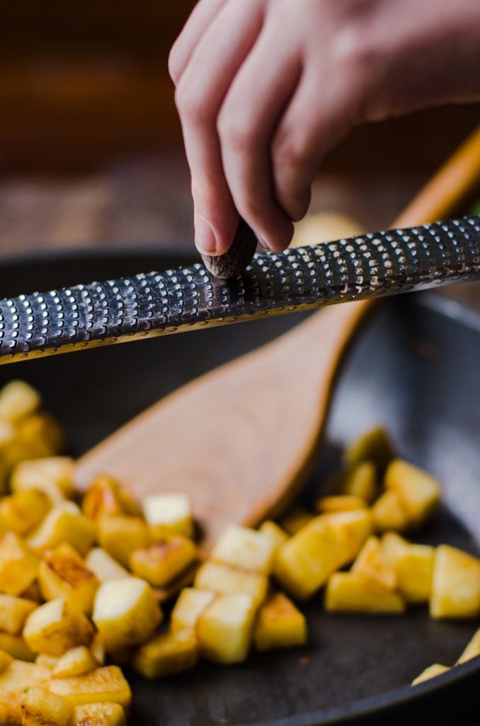 A hand grating whole nutmeg into a pan.