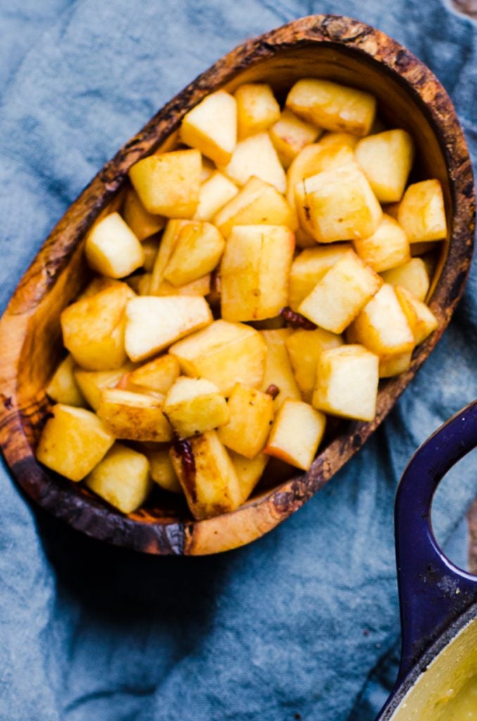 Overhead view of cooked apples in wooden bowl on a blue napkin.