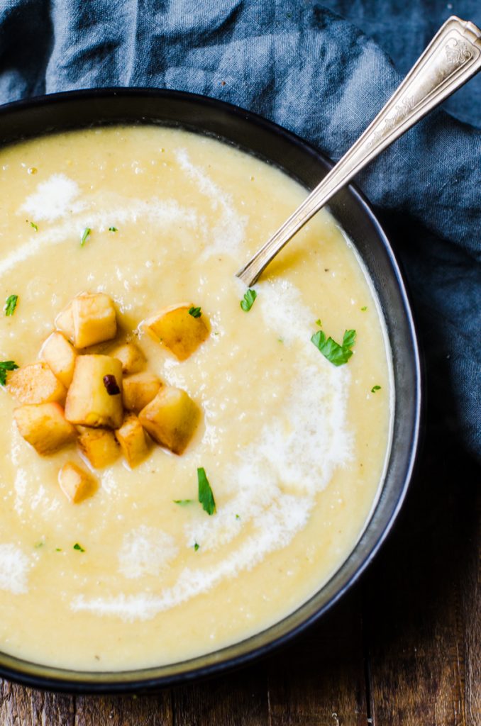 A spoon coming out of a black bowl of creamy parsnip soup.