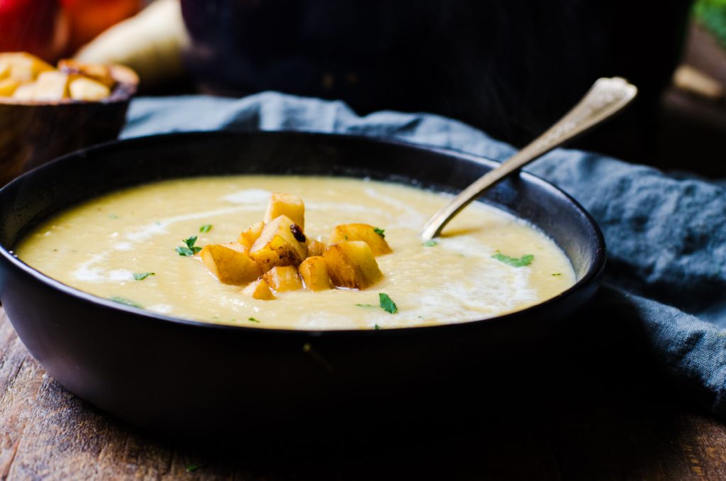 A spoon coming out of a black bowl of parsnip soup.