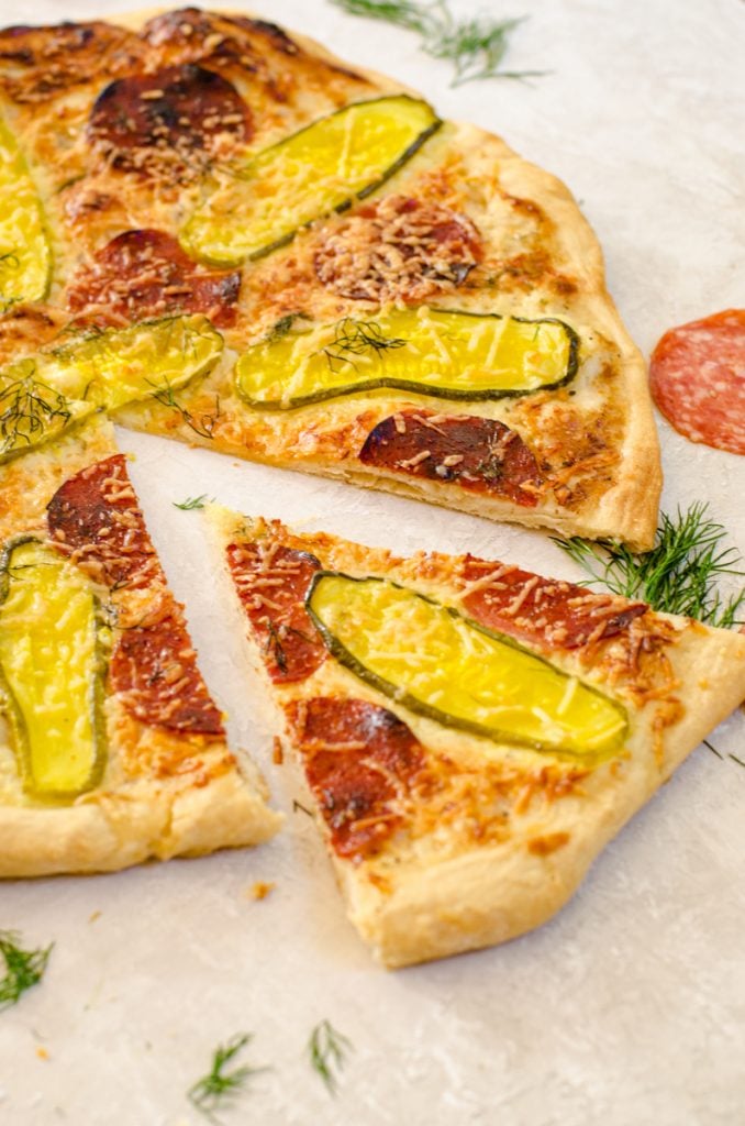 A slice of dill pickle pizza coming away from the whole pie.