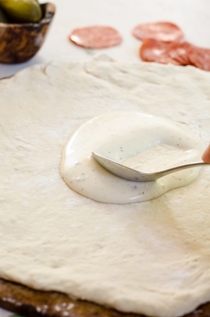 A spoon spreading ranch on dough.