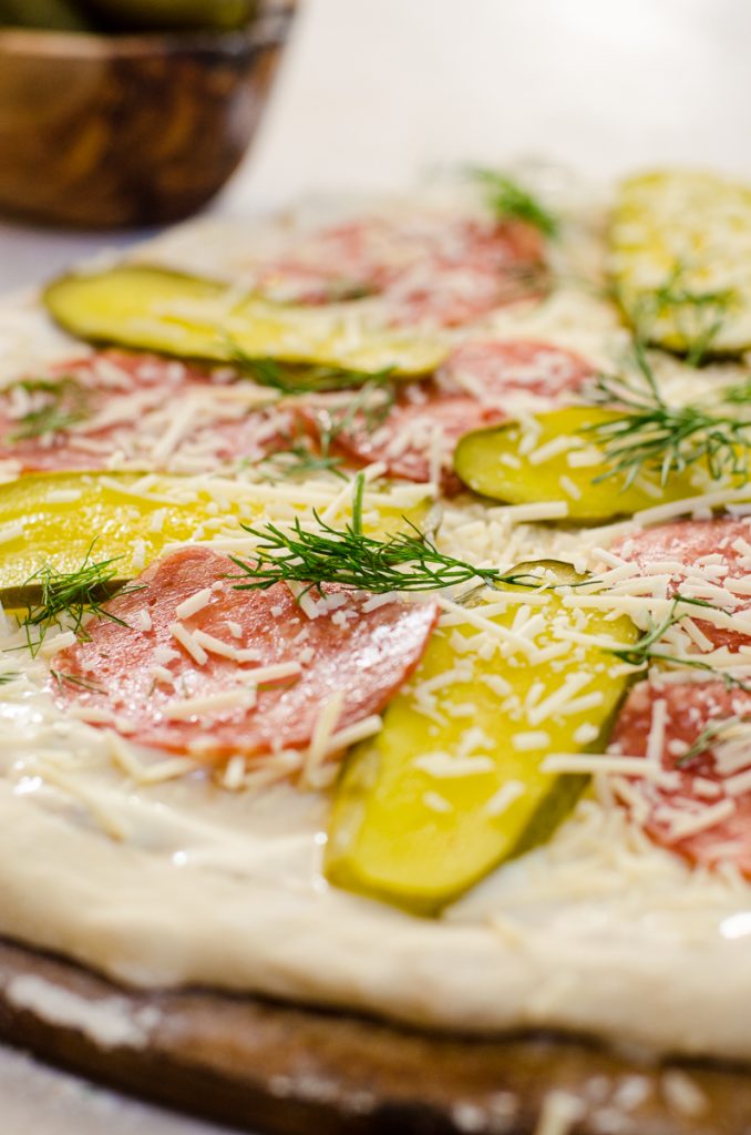 Close up of pickles and salami with cheese sprinkled on it.