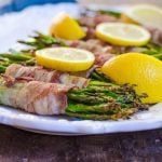Close up of bacon wrapped asparagus on a white tray garnished with lemons