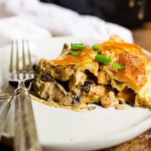 A slice of chicken and mushroom pie on a plate with a fork and knife next to it.