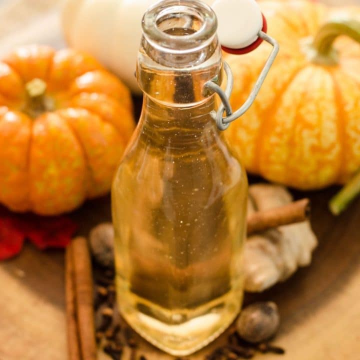 A bottle of homemade pumpkin spice syrup in front of decorative pumpkins.