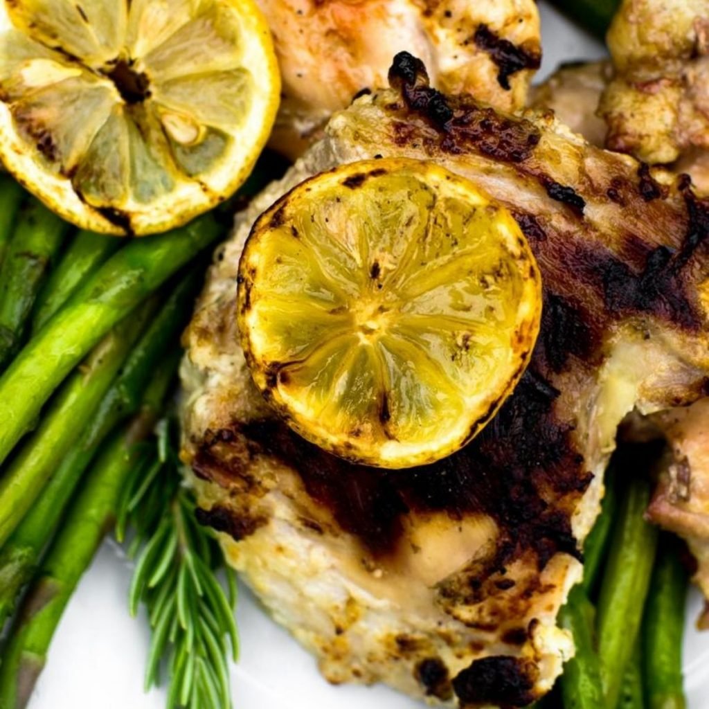 Close up of a grilled lemon on chicken next to asparagus.