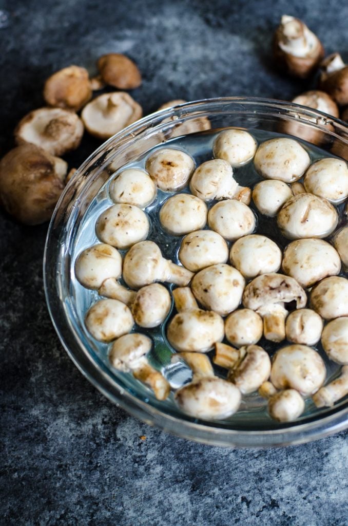 A bowl of water with white button mushrooms getting ready to be washed.