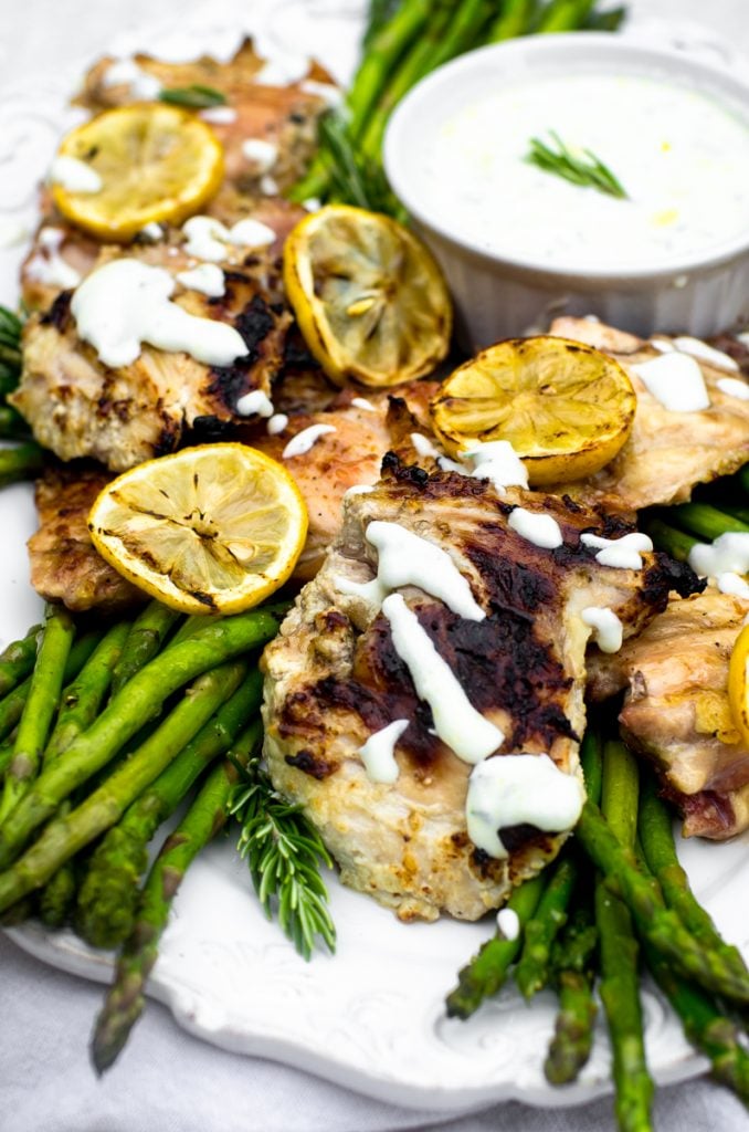 Yogurt sauce drizzled over grilled chicken on a white tray.