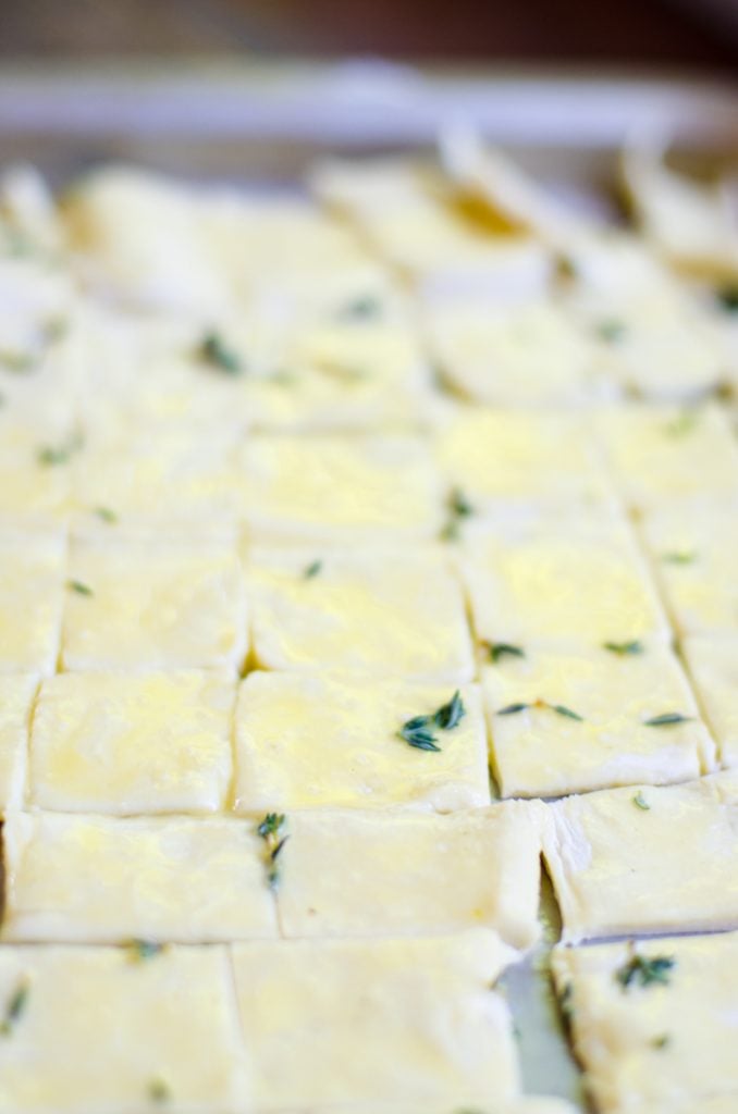 A sheet pan of cut puff pastry with fresh thyme sprinkled on it.