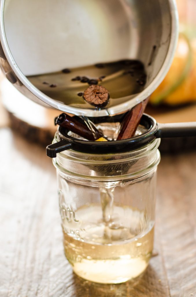 A pot pouring pumpkin spice syrup through a strainer into a jar.