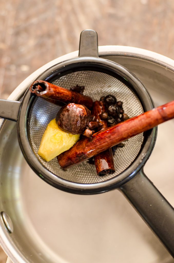 Strained whole spices above a pot.