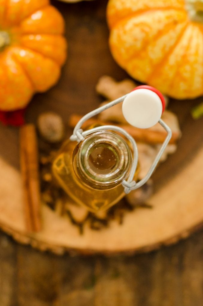 Overhead view looking into a bottle surrounded by pumpkins and spices.