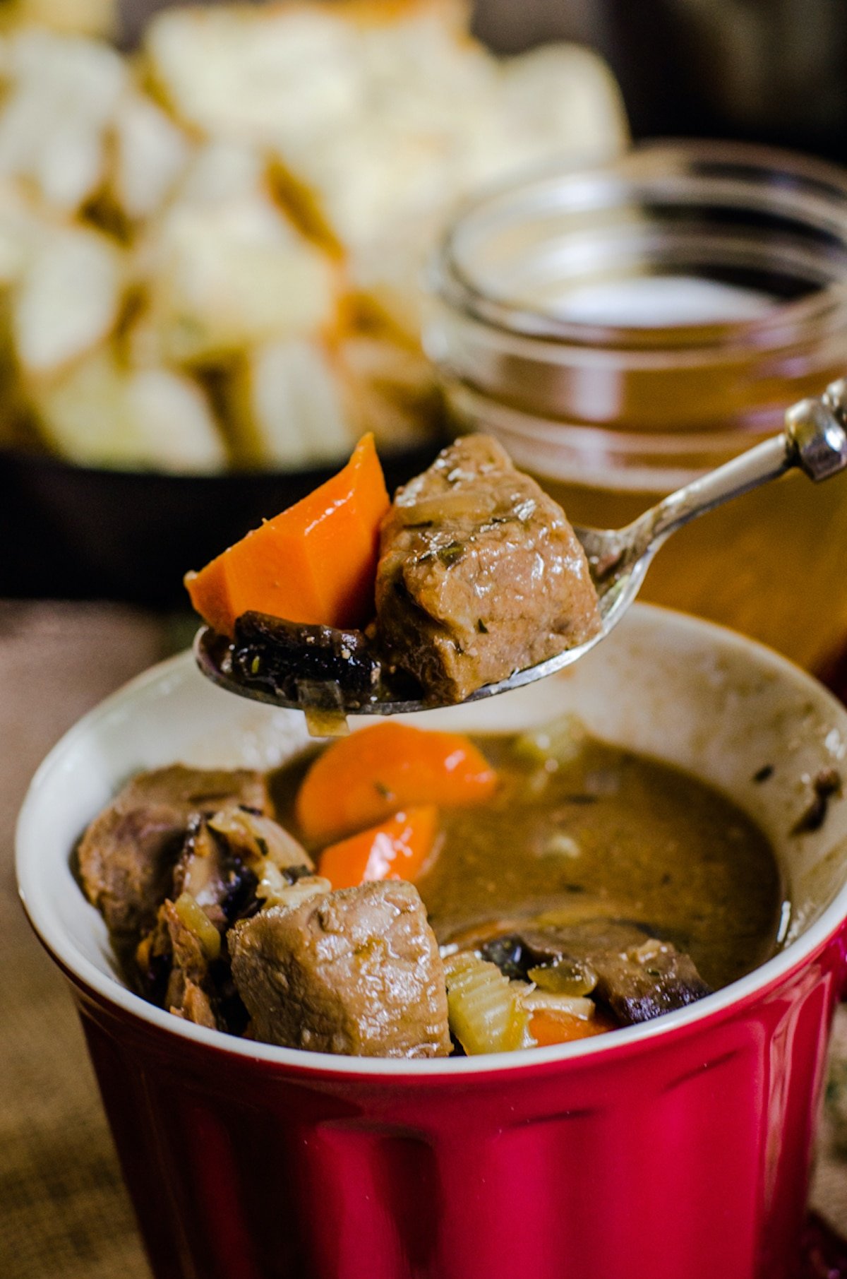 A spoon lifting beef and vegetables out of steak and ale soup.