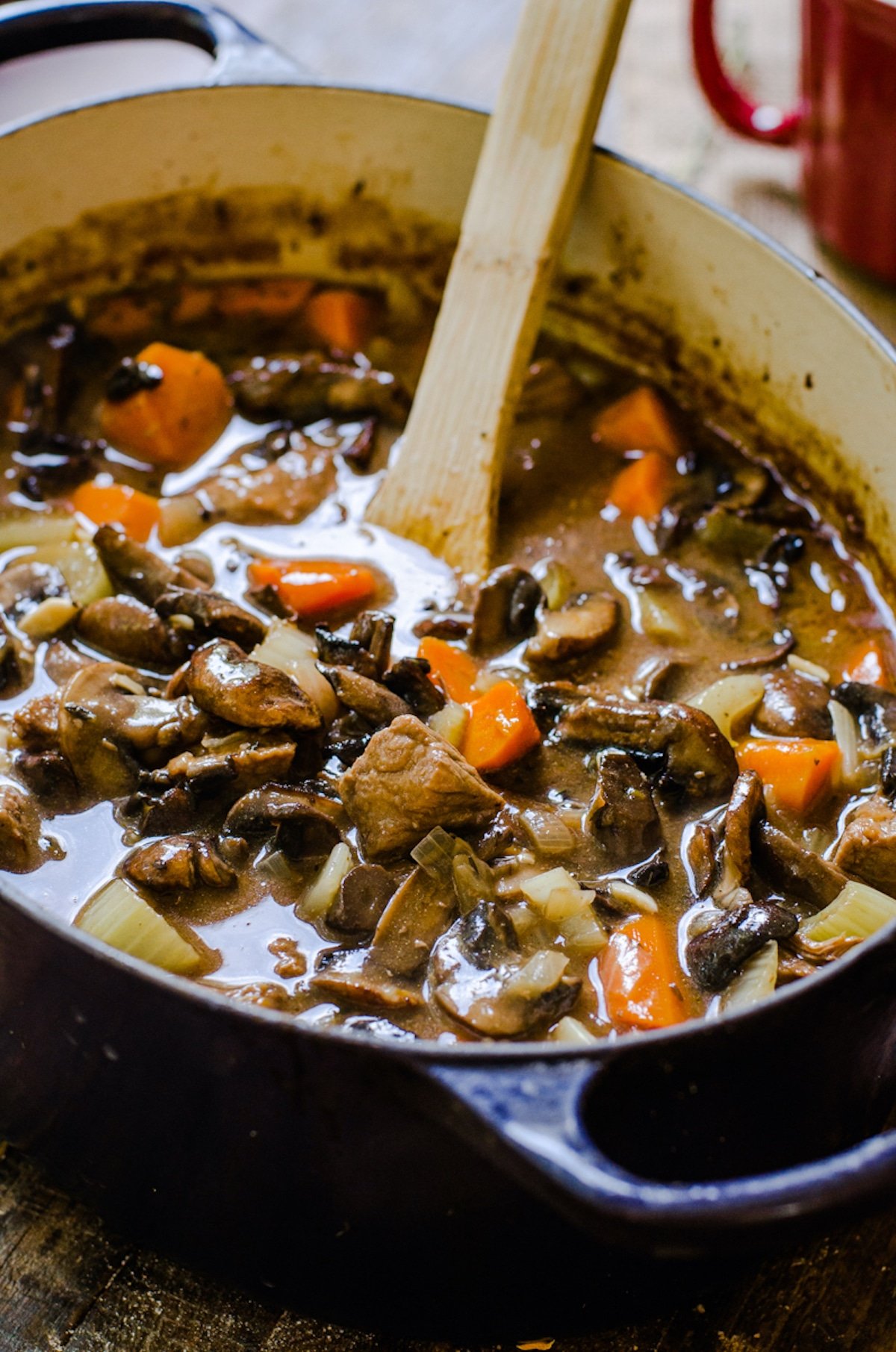 A wooden spoon coming out of a pot of hearty soup.