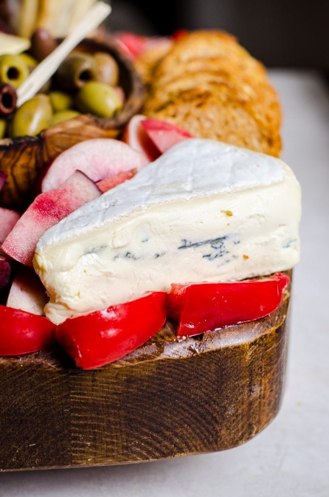 A wedge of blue cheese surrounded by fresh tomatoes on a summer cheese board.