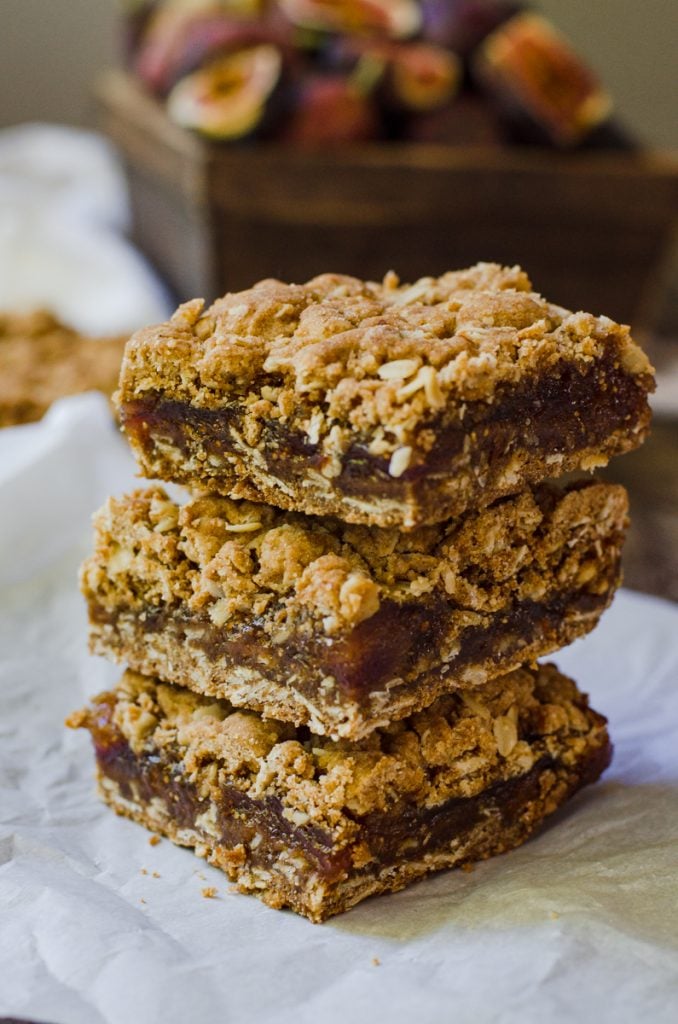 A stack of three fig bars with a box of fresh figs in the background.