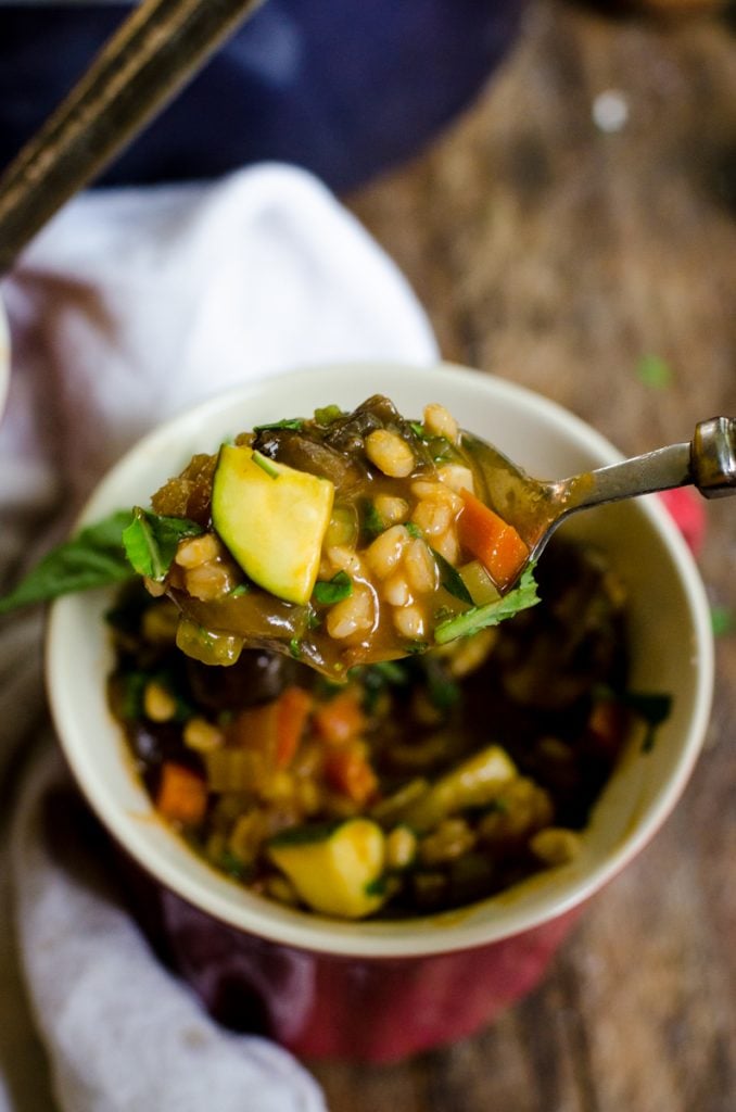 A spoon pulling a bit of vegetable barley soup out of a bowl.