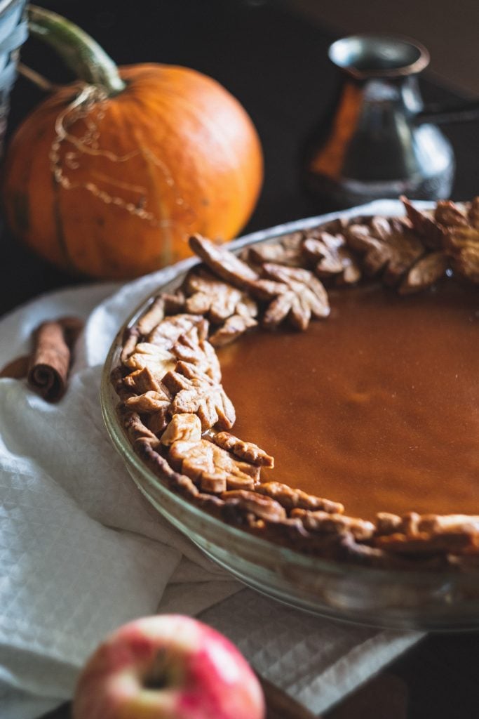 A decorated pumpkin pie in front of a fresh pumpkin.