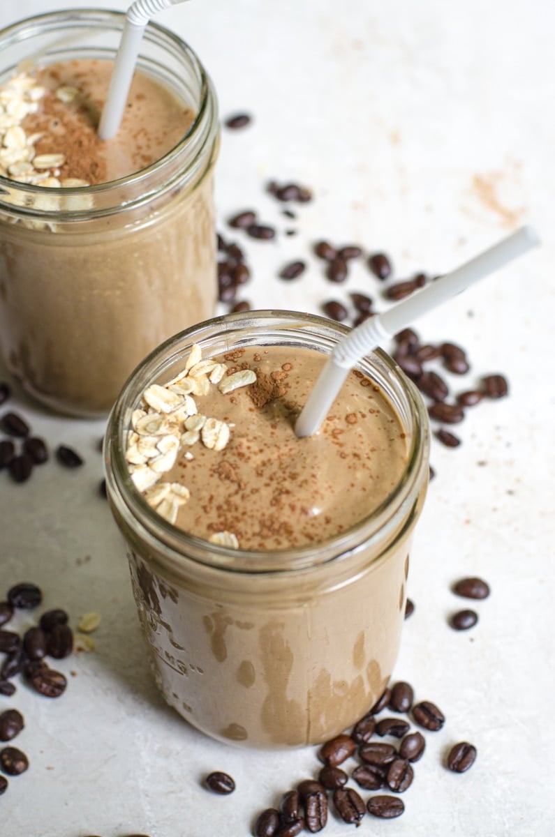 Two coffee smoothies with straws next to whole coffee beans.