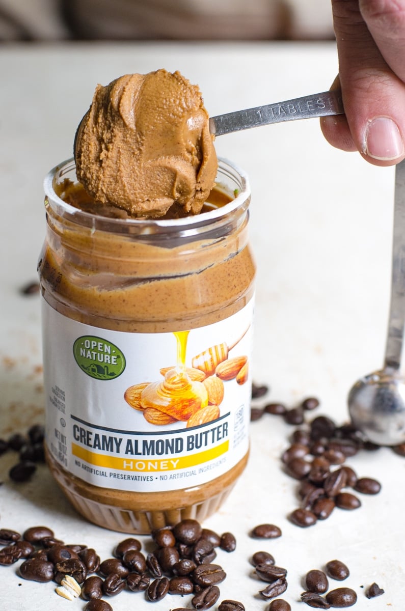 A hand pulling a Tablespoon of almond butter with honey from the jar.