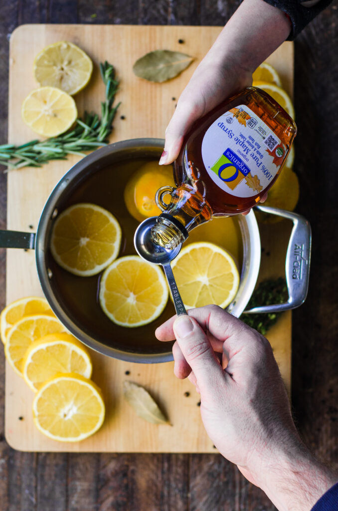 Hands measuring maple syrup into apple juice brine.