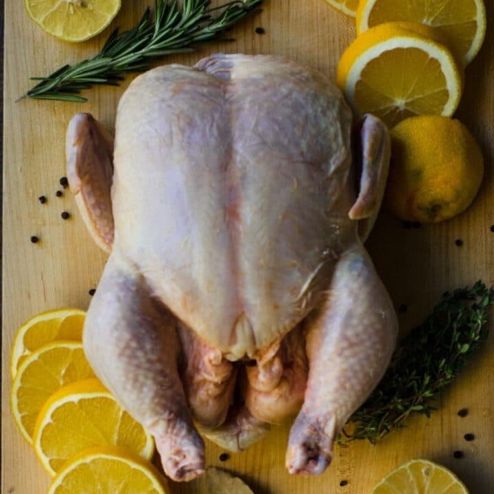 Raw chicken on a cutting board next to orange slices and herbs.