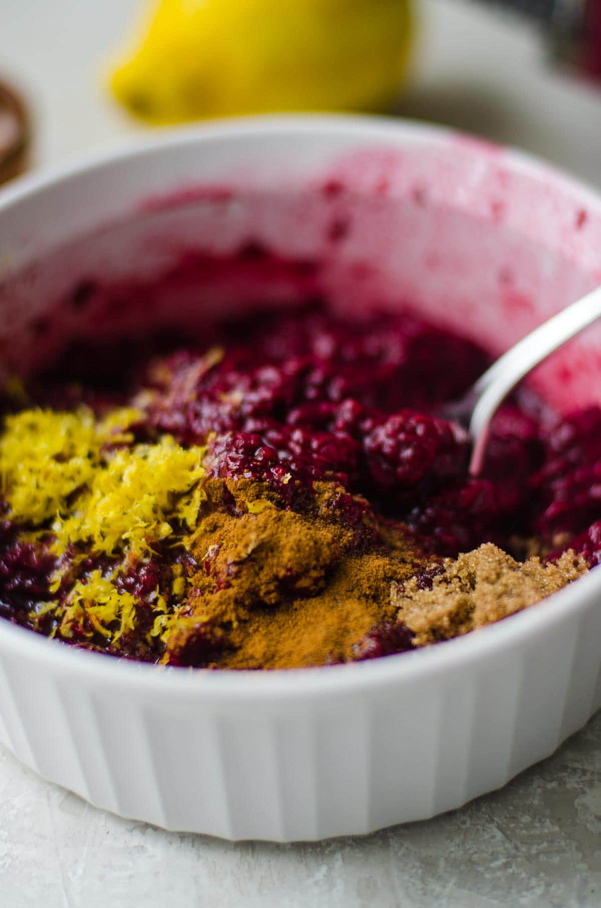 A white bowl of thawed frozen berries, lemon zest, and spices.