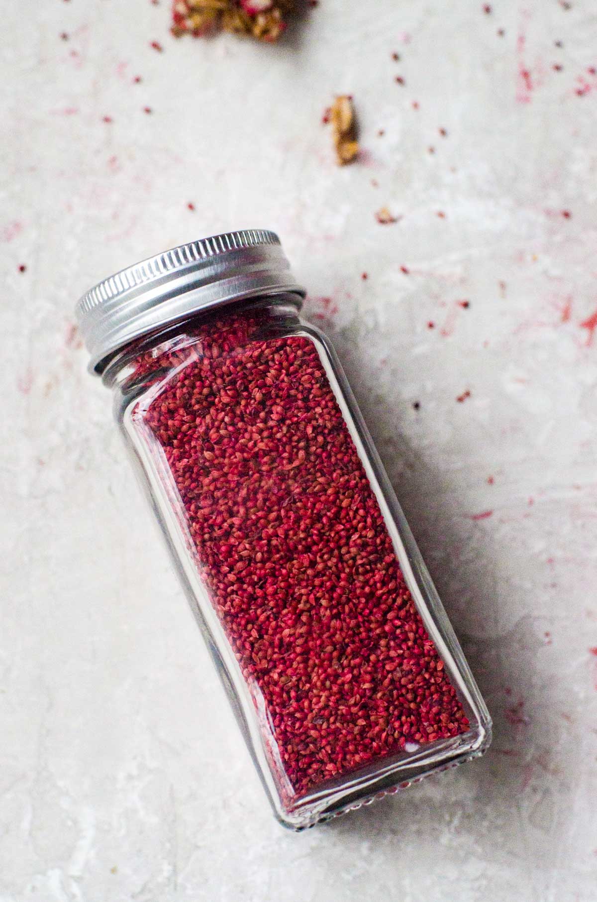 A clear spice container of red cranberry seeds.