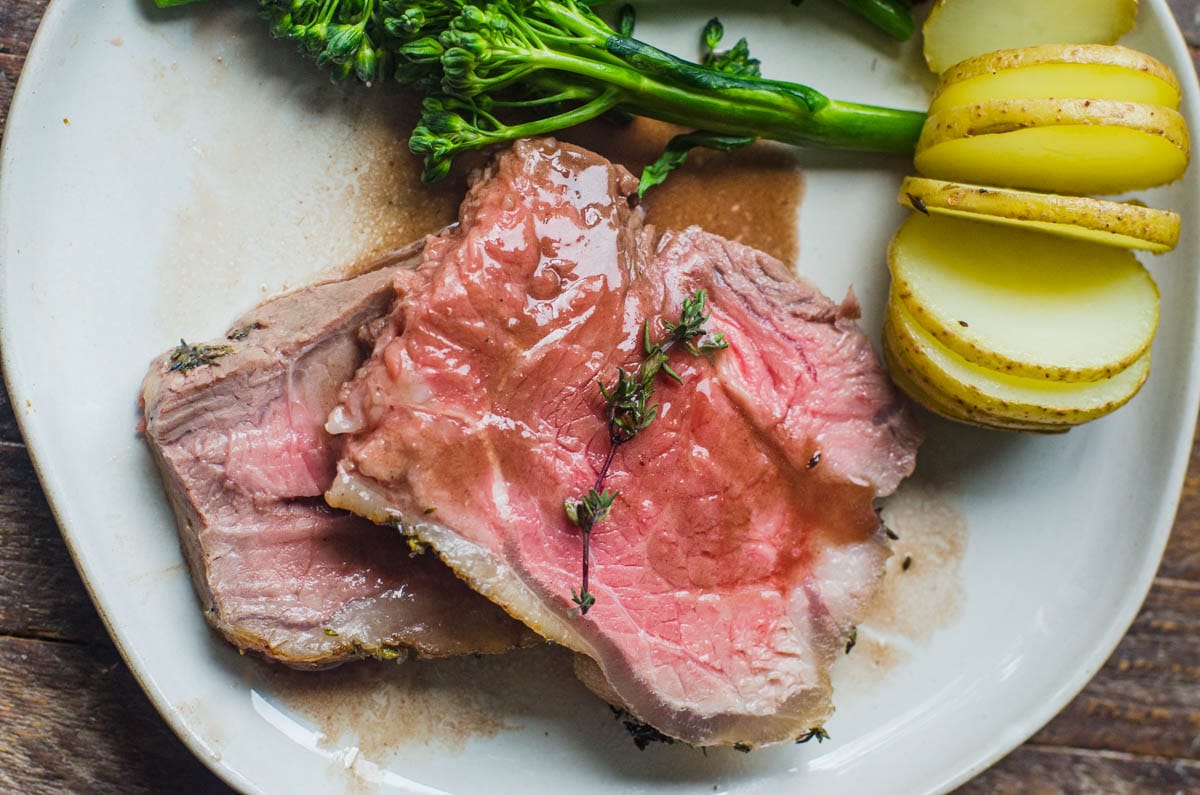 Two slices of New York striploin roast on a plate with potatoes and vegetables