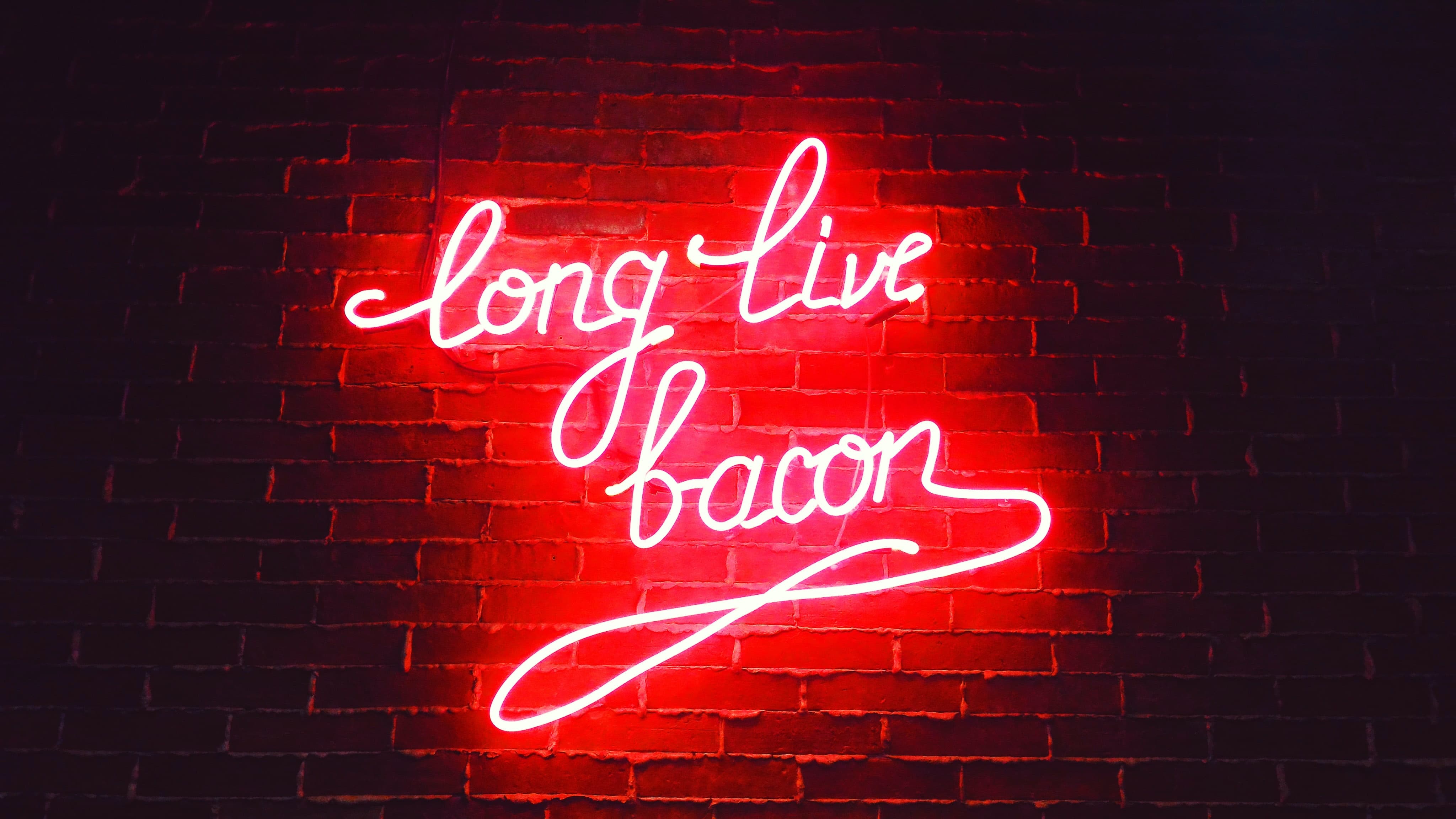 A neon sign on brick way saying "long live bacon" in red cursive.