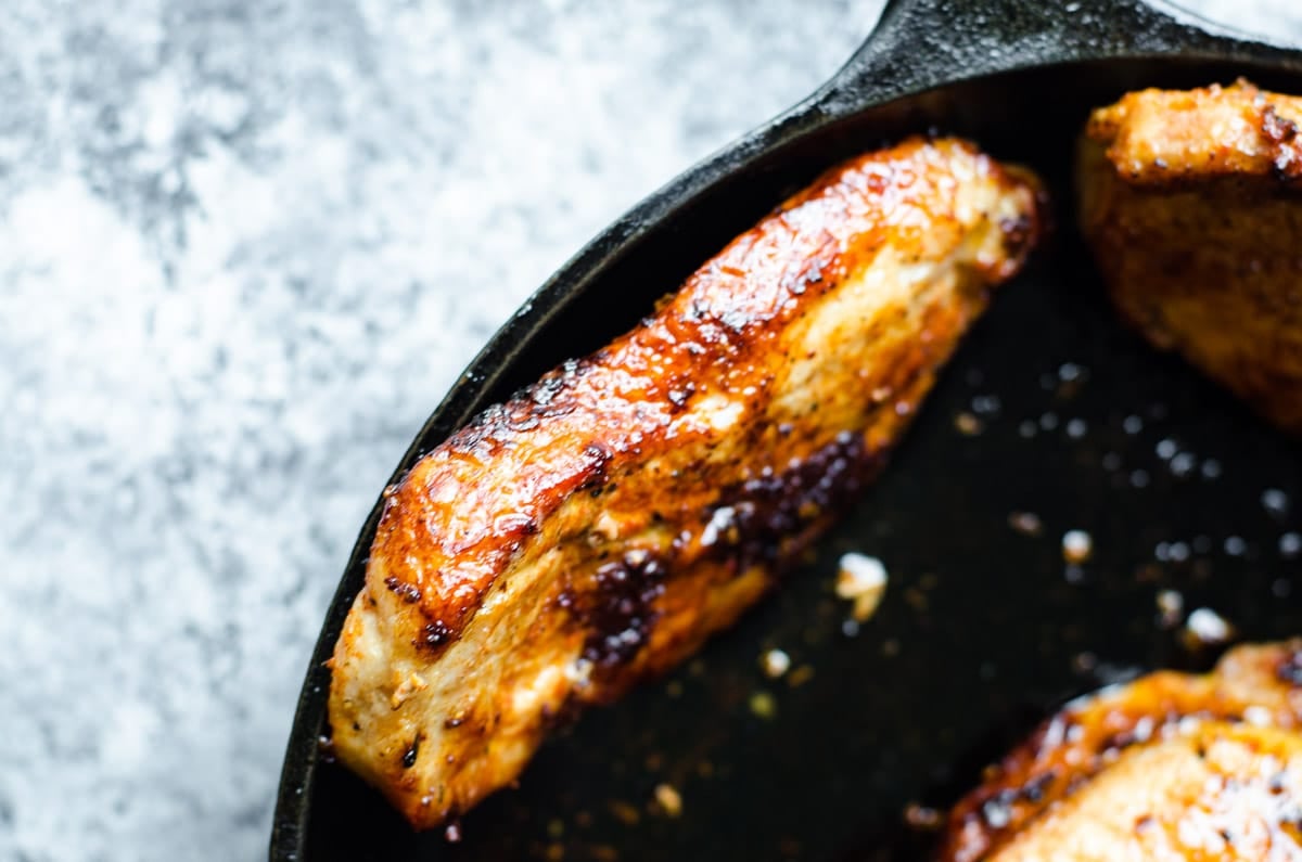 A pork chops standing up in the pan to cook the fatty edge.