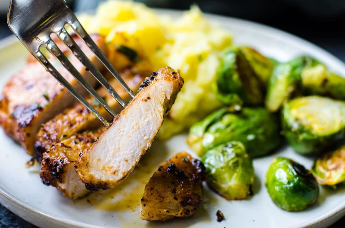 A fork picking up a bit of pork chop from a plate.