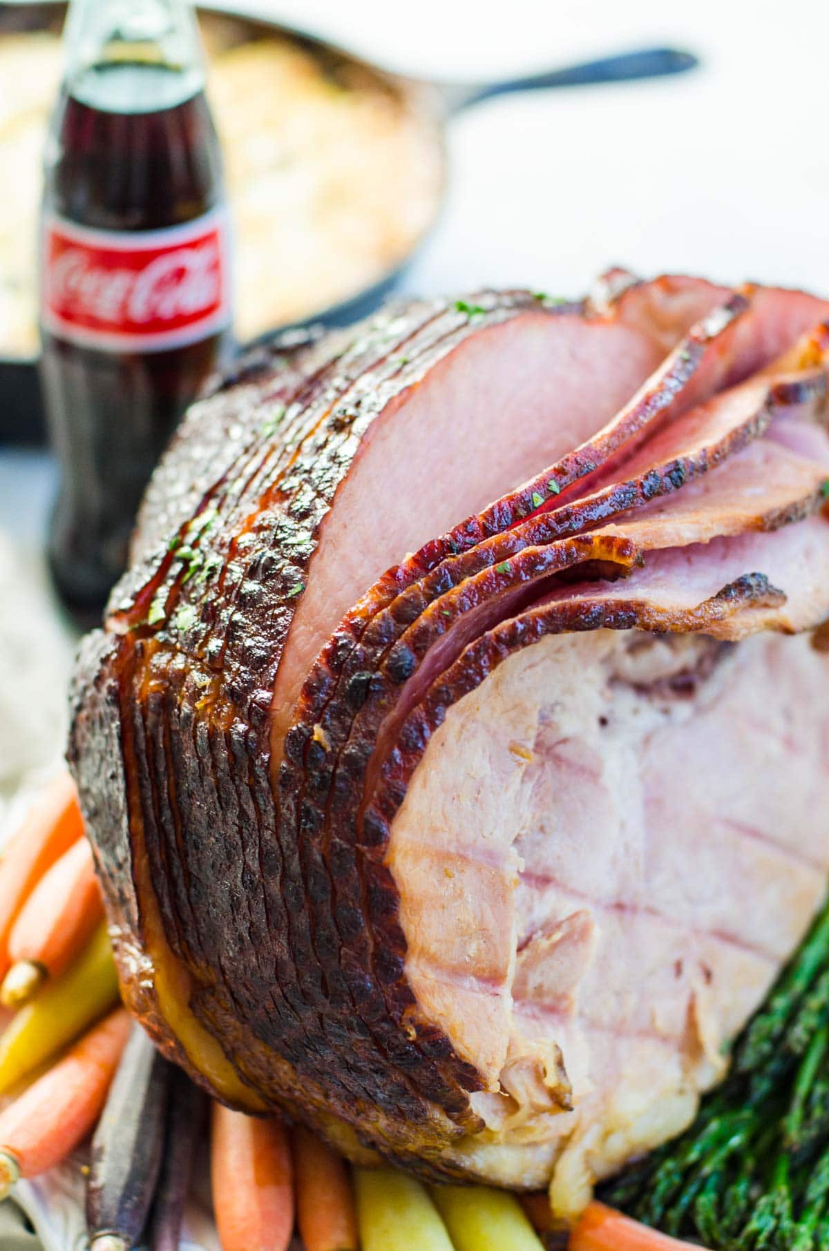 A cooked sliced ham in front of a bottle of coca cola.