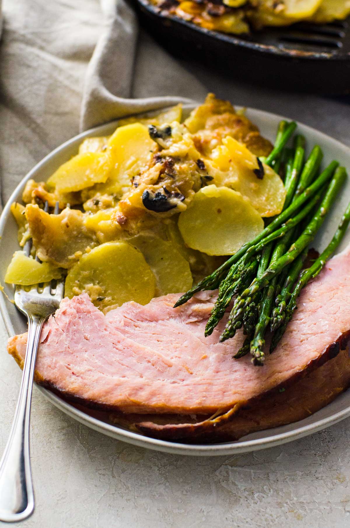 A plate of ham, asparagus, and scalloped potatoes with a fork.
