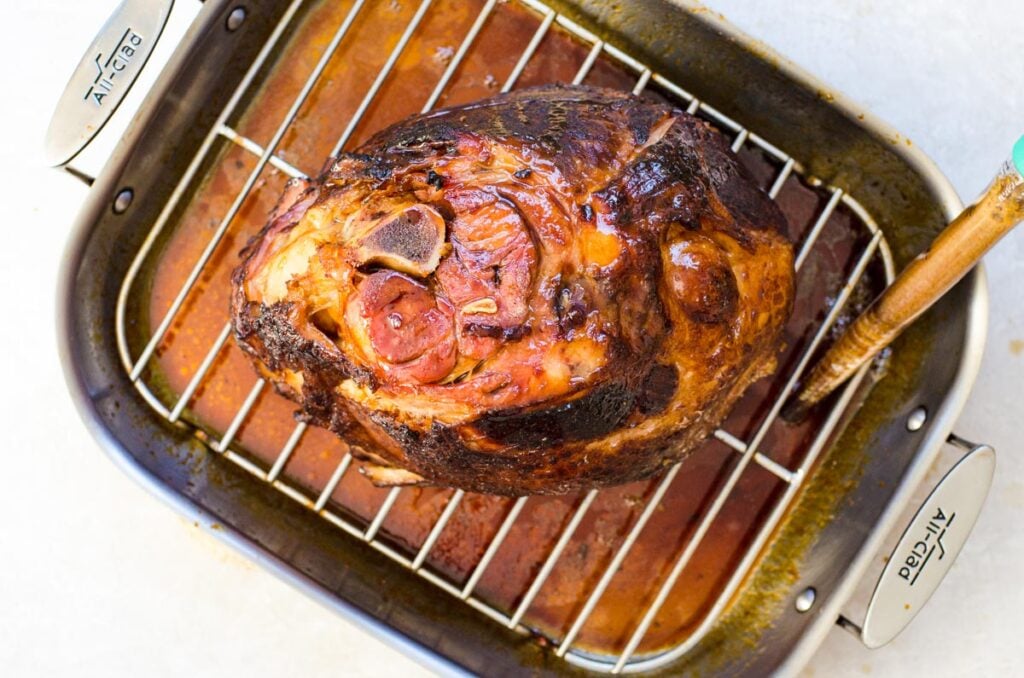 Overhead view of cooked glazed ham with a baster pulling up juices.