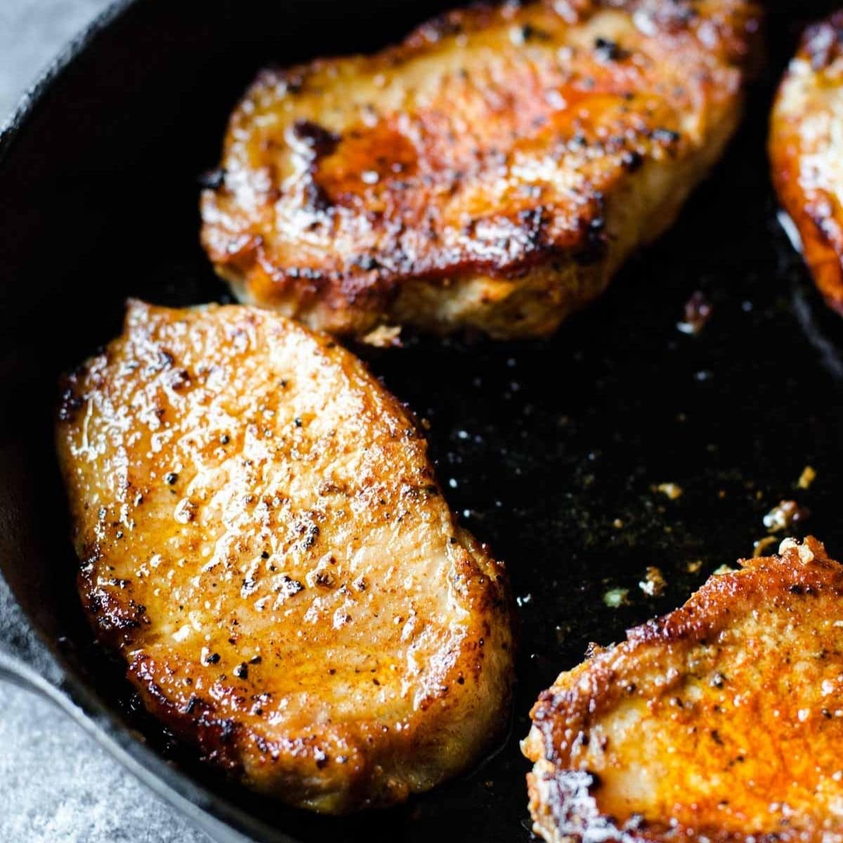 Seared golden brown pork chops in a cast iron pan.